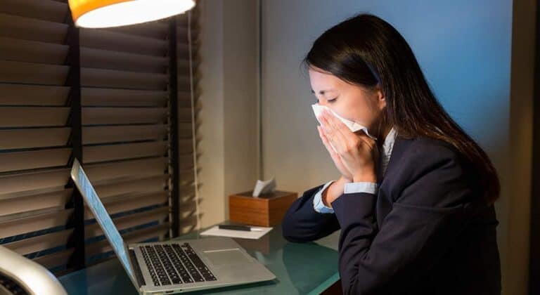 woman having an allergic reaction in her college dorm as she sneezes into a tissue