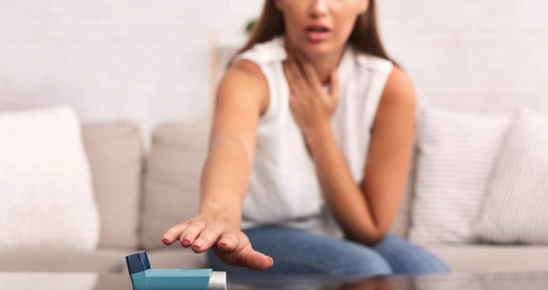 a woman with asthma who is having an attack reaching for her inhaler.