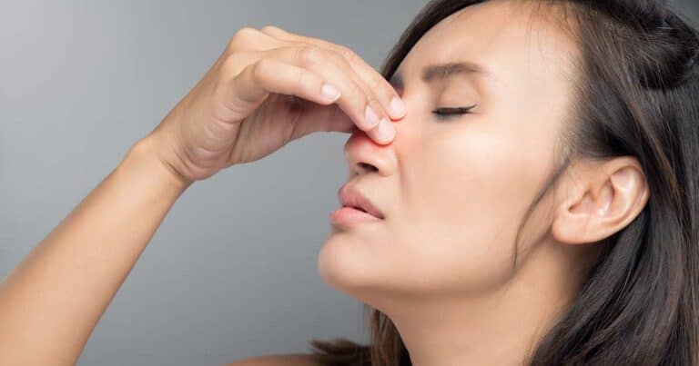 a woman with sinus pressure holding her nose with her eyes closed