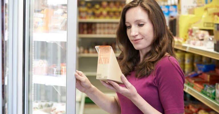 Woman standing in the aisle of the supermarket, reading the food label on a pre-made sandwich. She's checking for food allergens.