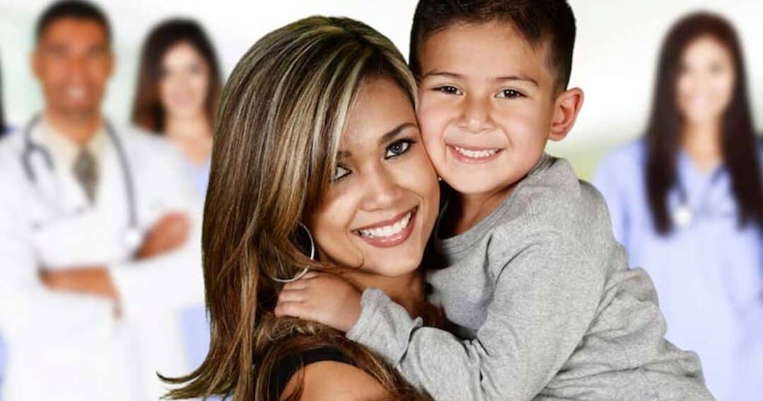 Smiling woman holding a young boy, both looking at the camera. The background shows blurred images of medical professionals, including doctors and nurses.