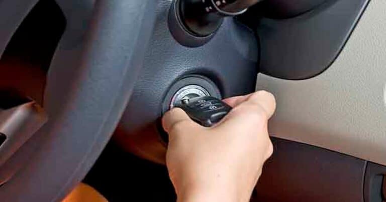 A hand is turning a car key in the ignition of a vehicle, with a close-up view of the steering wheel and dashboard.