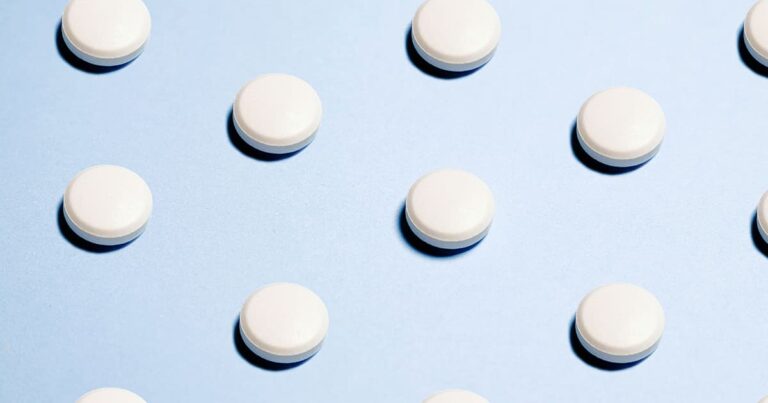 Round white tablets are evenly spaced in a grid pattern on a light blue background.