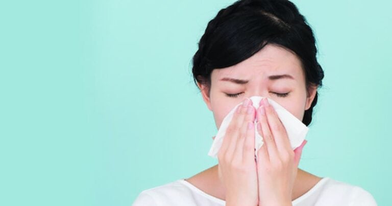 woman with dark hair blowing her nose due to allergies