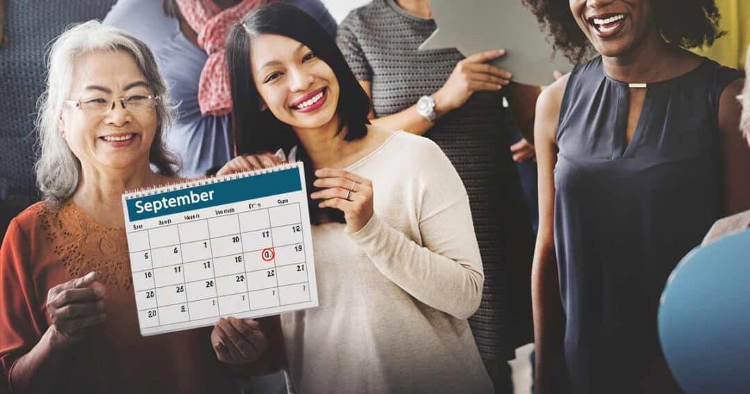 A group of smiling women stand together, with one holding a calendar turned to September. A date is circled in red, and the group appears happy and celebratory.