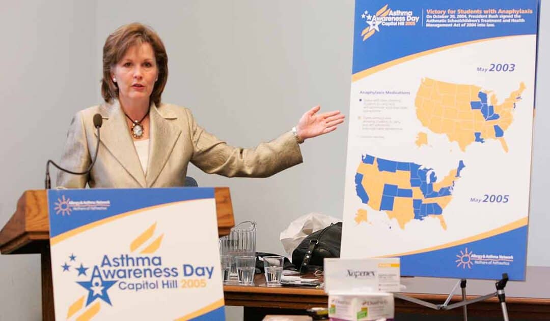 A woman stands at a podium labeled "Asthma Awareness Day Capitol Hill 2005," gesturing toward a large board displaying asthma statistics and maps of the U.S. in a conference room setting.