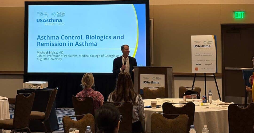 A speaker stands at a podium presenting to an audience at the USAsthma Summit 2025. A slide on the screen reads “Asthma Control, Biologics and Remission in Asthma” by Michael Bilasa, MD.