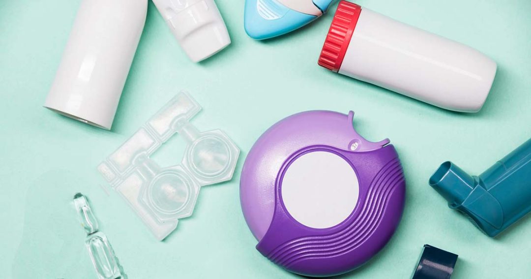 Inhaler Confusion 1 A variety of asthma inhalers and medication devices, including canisters, blister packs, and a purple round inhaler, are arranged on a light blue surface.