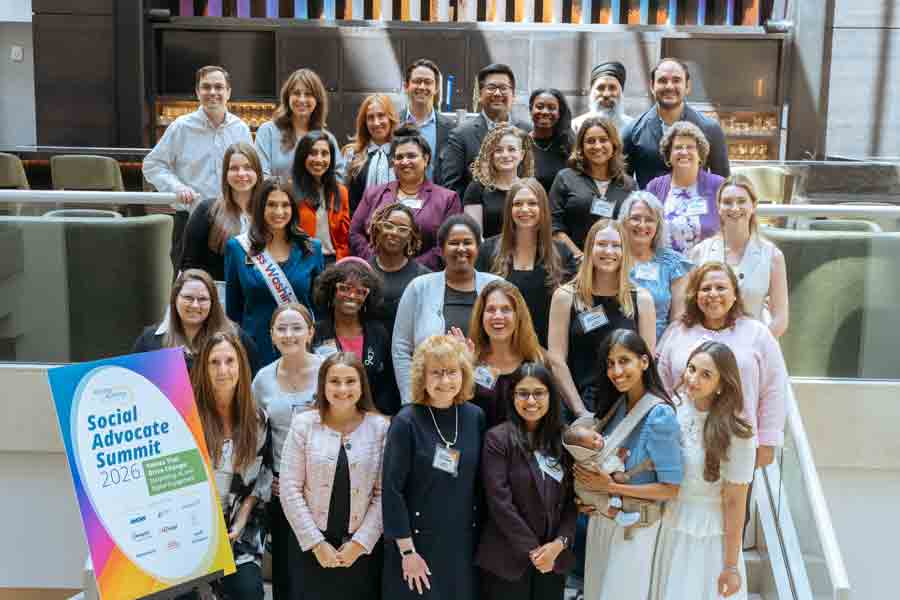A diverse group of people posing and smiling together at the Social Advocate Summit 2026, indoors, with a colorful event sign in the foreground and modern decor in the background.