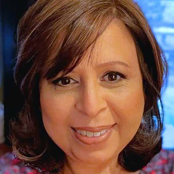 A woman with shoulder-length brown hair and brown eyes smiles at the camera. She is indoors with a softly blurred background.