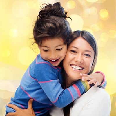 A young girl smiling and hugging her mother.